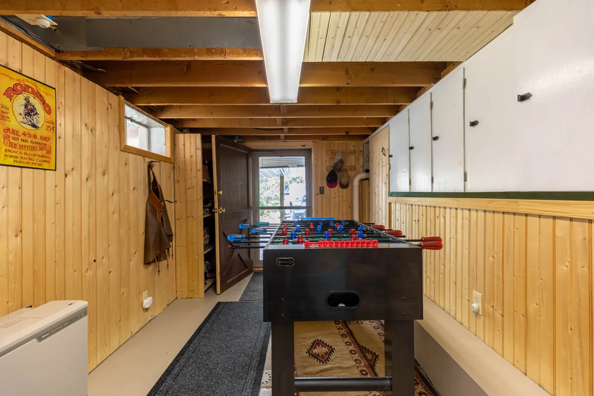A cozy, wood-paneled game room featuring a foosball table positioned near a window and door, inviting playful competition and social gatherings. The room’s natural light and rustic decor create a welcoming space for guests of all ages.