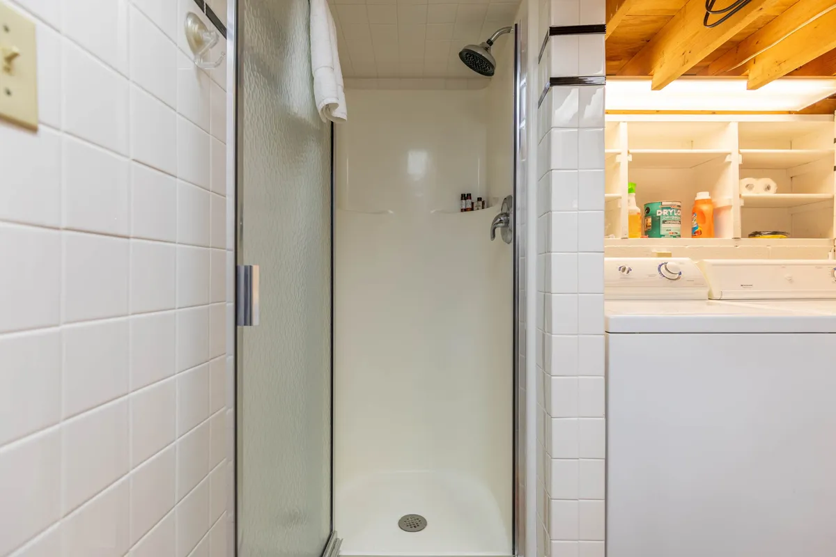 A practical laundry area with a washing machine, a separate shower enclosure, and shelves stocked with toiletries, all set against warm wood paneling. The setup emphasizes convenience and comfort for guests needing to freshen up after outdoor adventures.