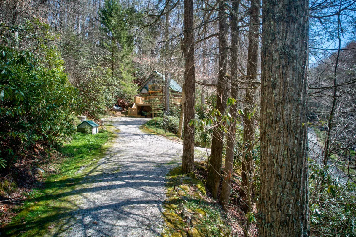 A gravel pathway winds through a wooded area, leading toward the cabin situated in the background. The scene exudes tranquility and invites viewers to imagine embarking on nature walks or beginning a sunrise hike directly from the property.