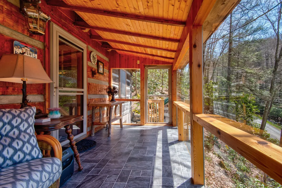 A cozy wooden porch featuring a decorative table and lamp, with inviting seating and a view through the railing to natural surroundings. The soft lighting and rustic elements evoke a peaceful mountain retreat, perfect for private moments or sipping morning coffee while enjoying the fresh air.