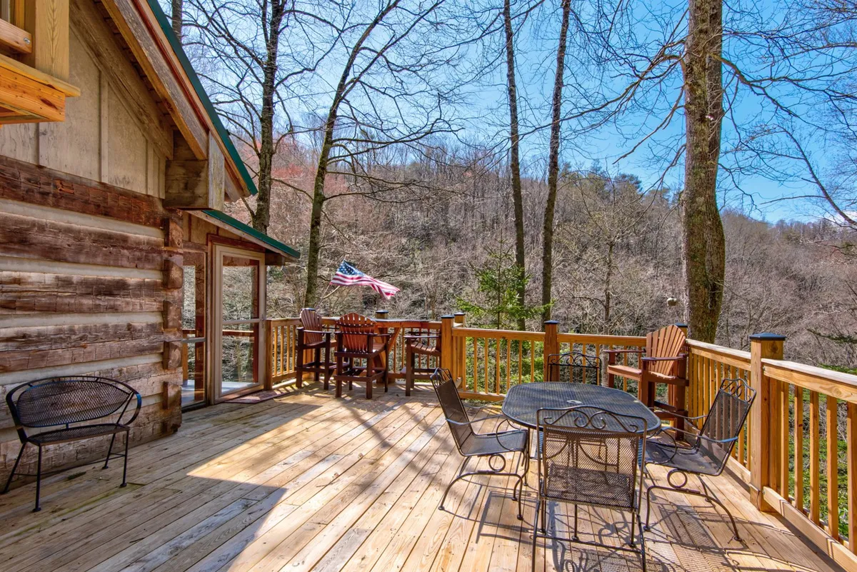 A spacious wooden deck with comfortable outdoor seating, an American flag, and a serene tree line in the background. The setup encourages relaxing, socializing, and enjoying the fresh mountain air—ideal for unwinding with pets after a day of adventure.