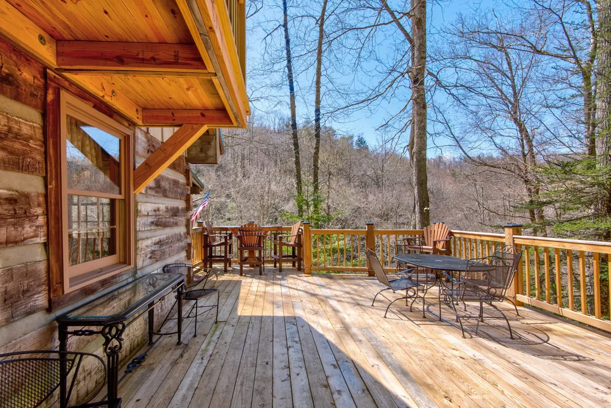 An exterior shot of a wooden deck with outdoor seating surrounded by lush trees and offering a distant mountain view. The deck suggests ample space for al fresco dining, relaxation, and social gatherings, capturing the essence of outdoor living tied to the Carolina sunroom.