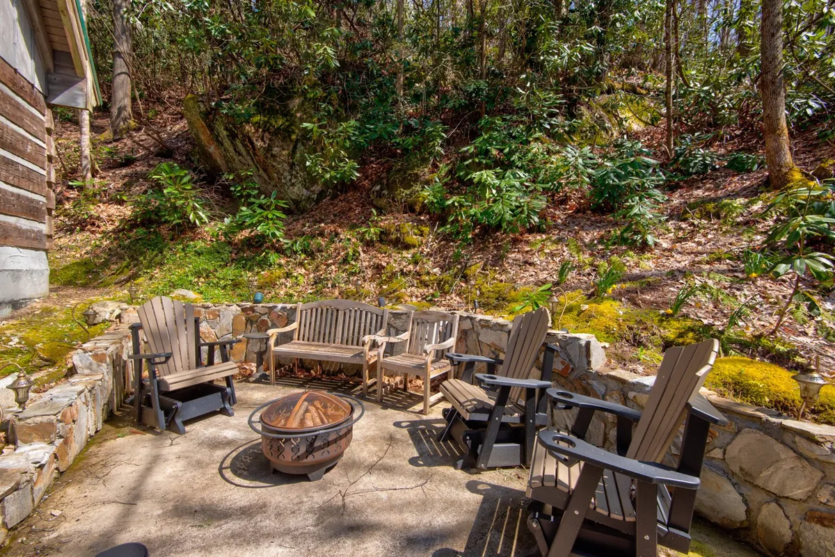 A stone firepit encircled by comfortable seating sits amid a natural backdrop of trees and open sky. The setup is inviting for evening gatherings, storytelling, or simply relaxing while enjoying the sights and sounds of the outdoors. The firepit looks ready for use, suggesting warmth and community under the stars.