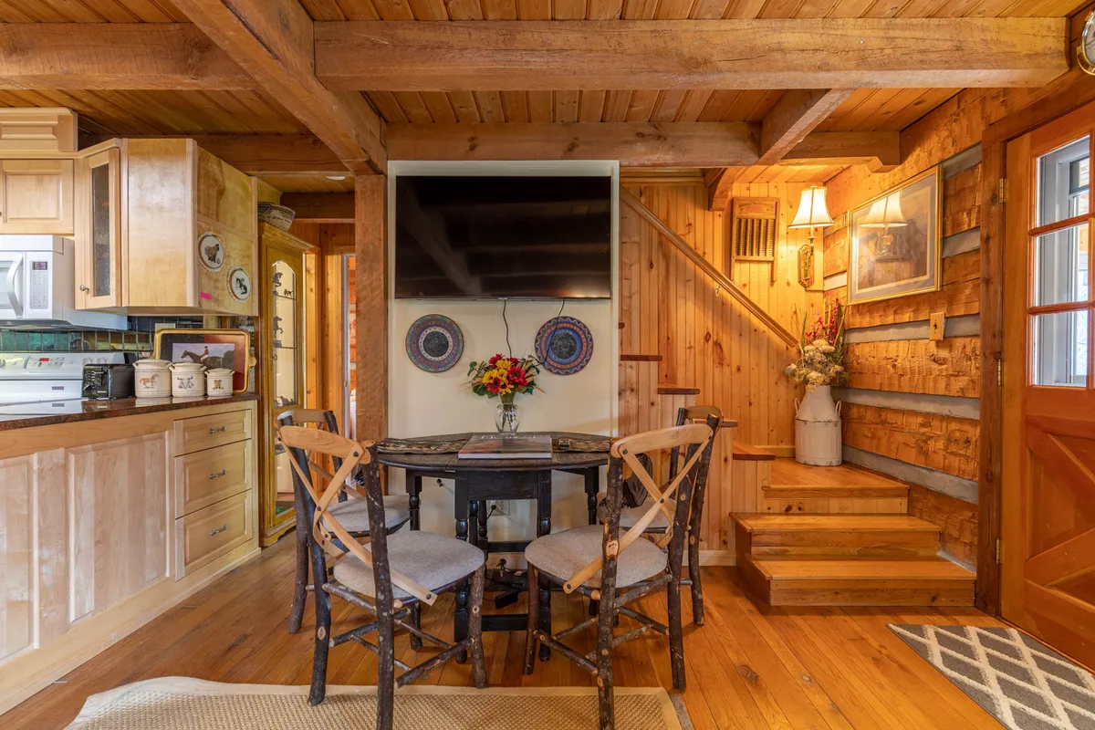 This view highlights the spacious dining table, staircase, kitchen cabinetry, decorative wall art, and a wall-mounted TV. The arrangement suggests a seamless flow between eating, socializing, and relaxing, with ample room for the whole group to gather.